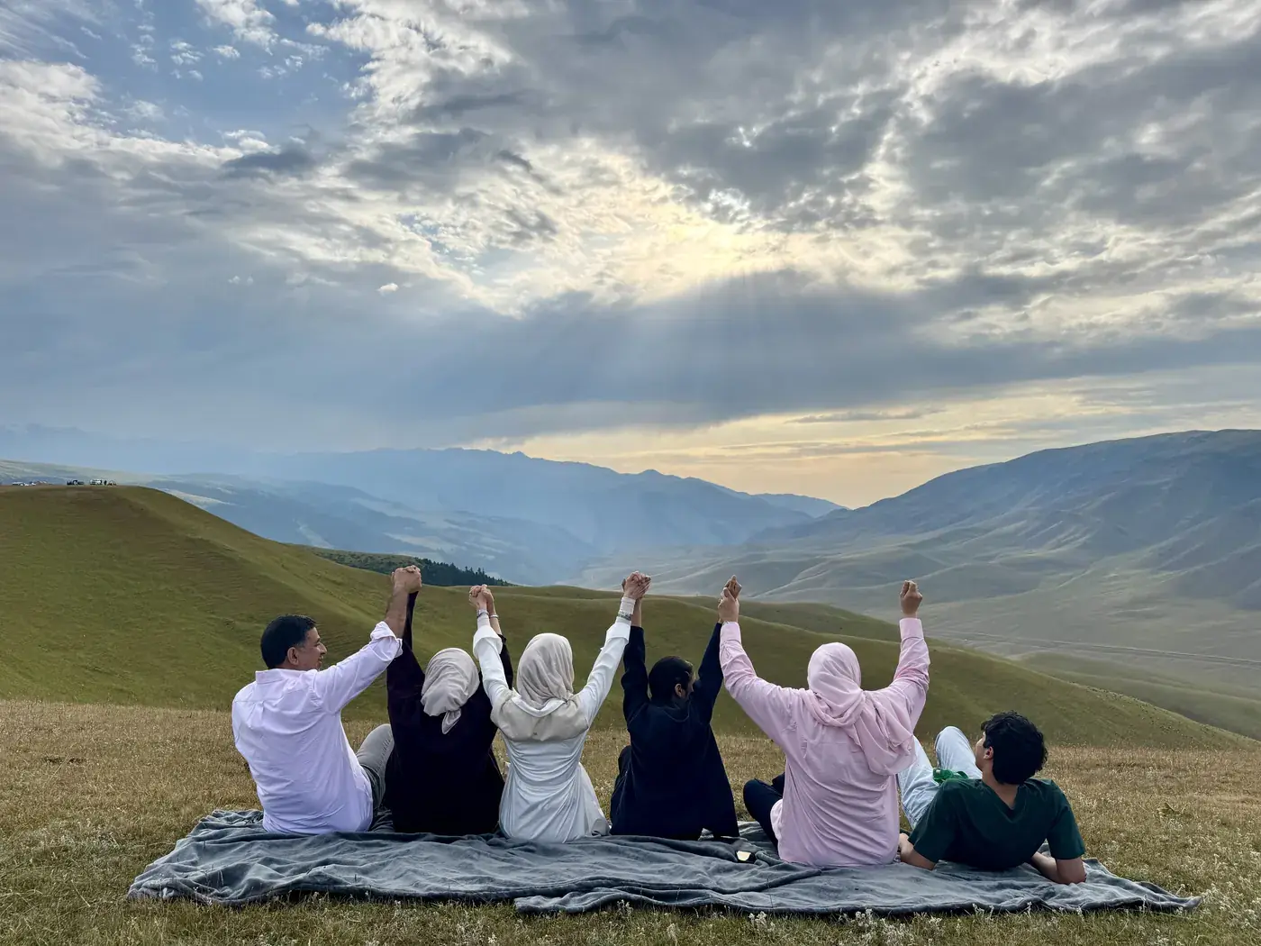 Travelers raising their arms above a green valley on the Assy Plateau