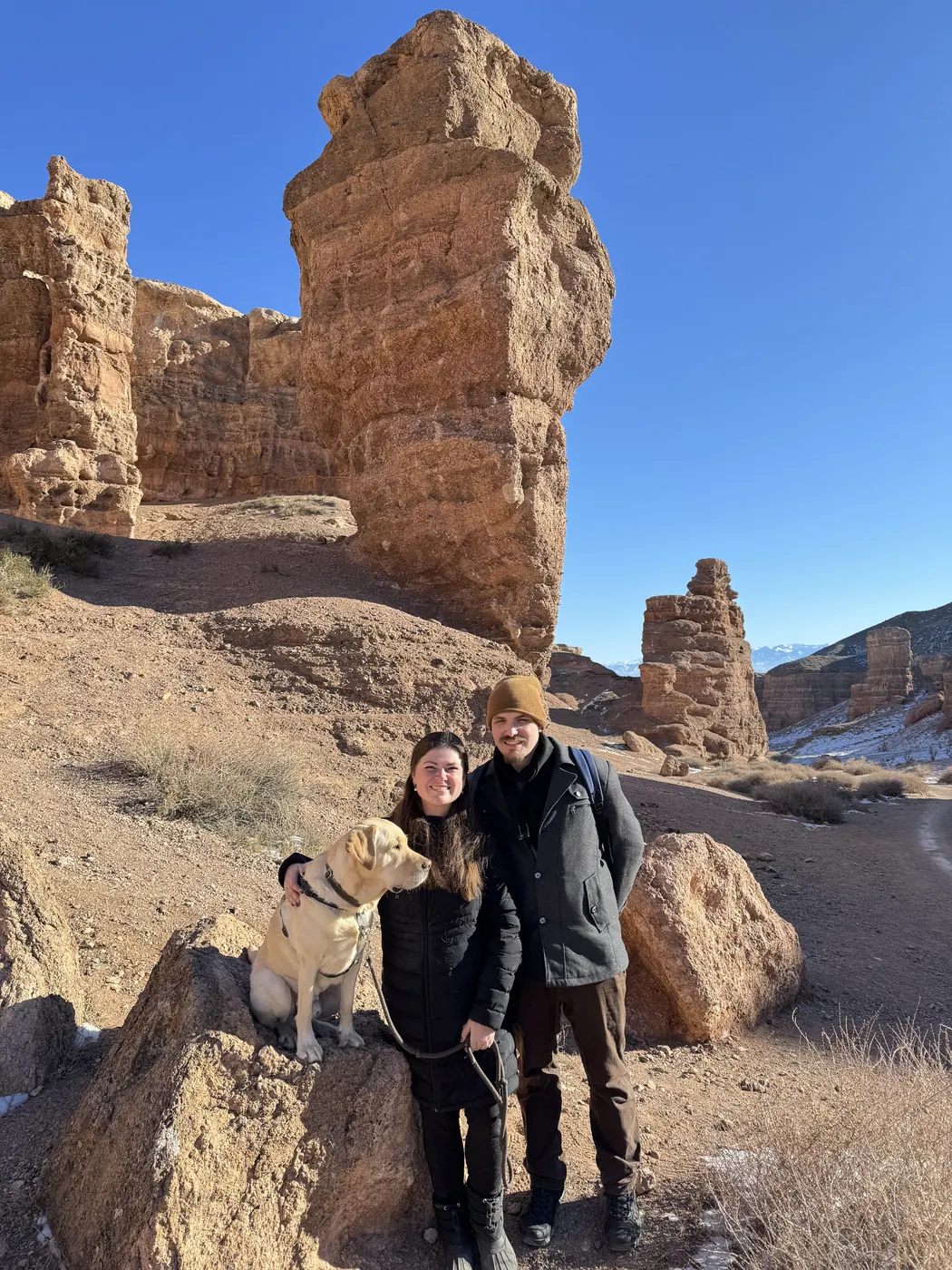 Two travelers and their dog among the rock towers of Charyn
