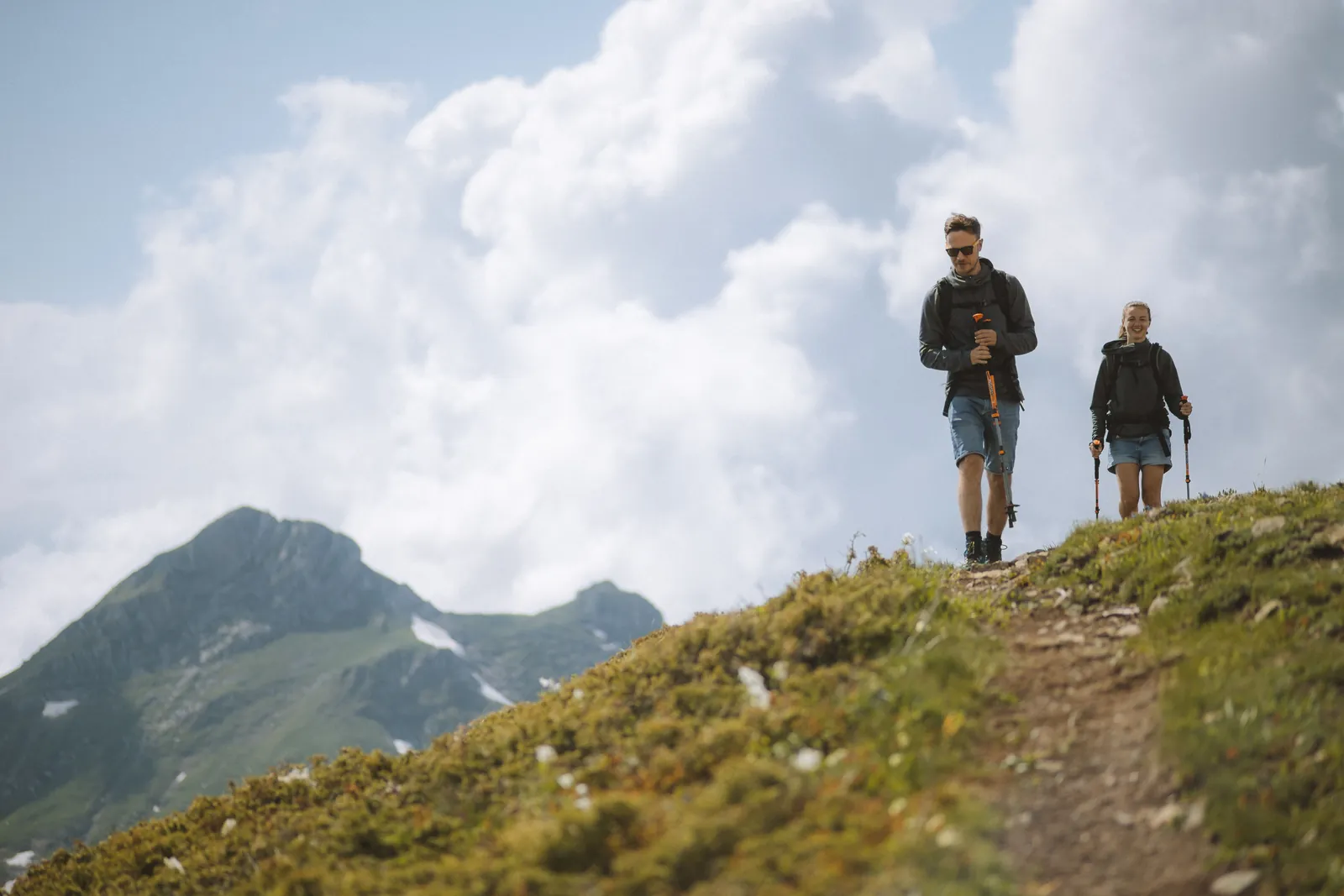 Two hikers with trekking poles on a grassy mountain ridge