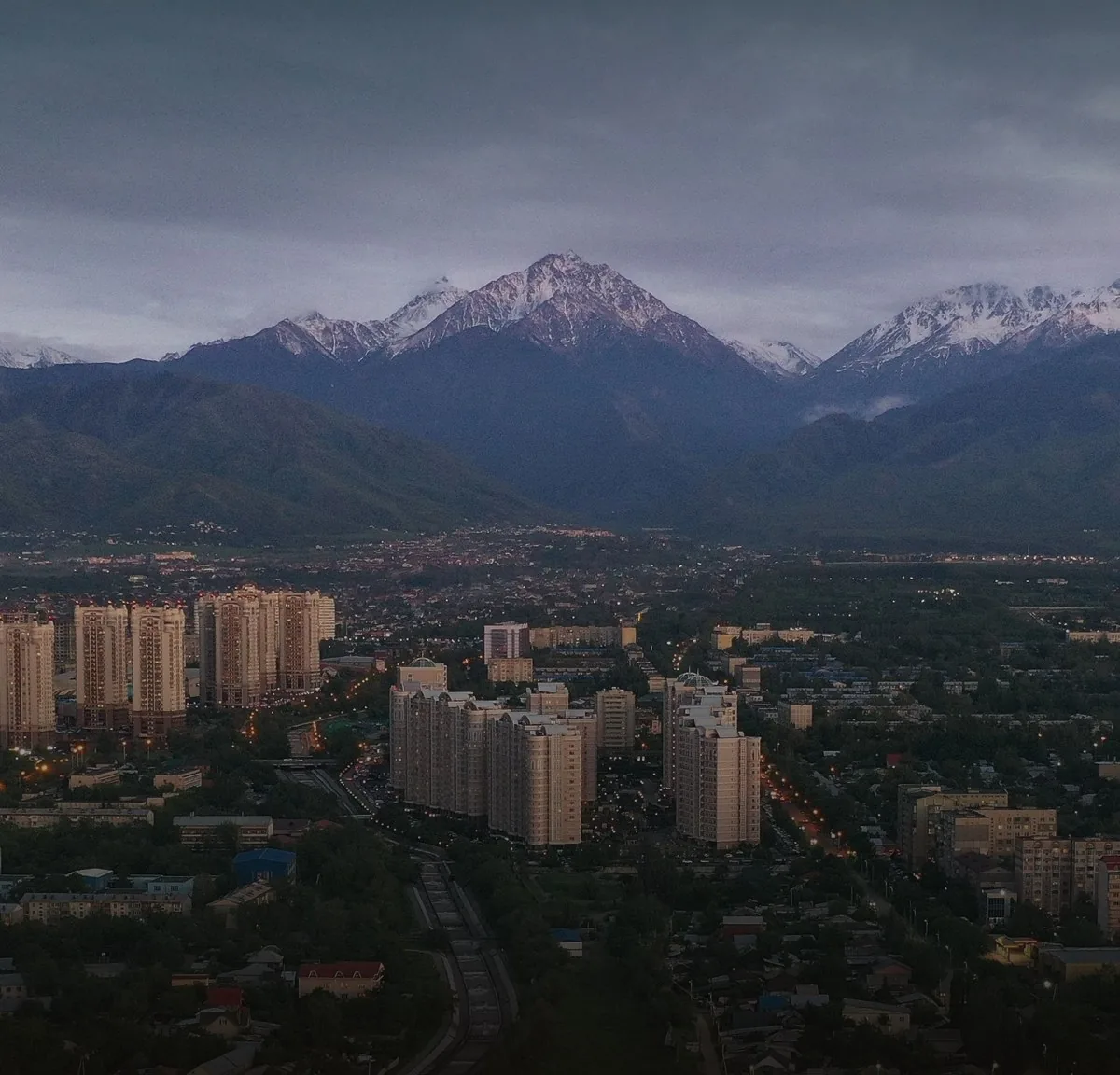 Almaty high-rises below the snowy mountains at dusk