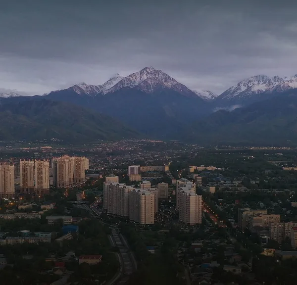 Almaty high-rises below the snowy mountains at dusk